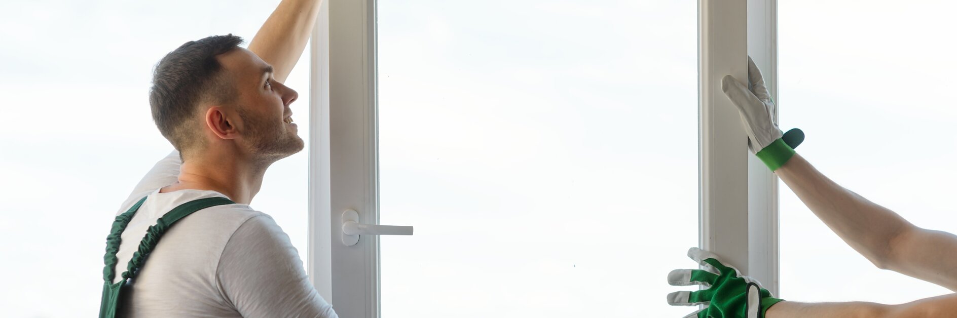 Photo of two workers installing a plastic window. Man holding a glass pane with a vacuum lifter.