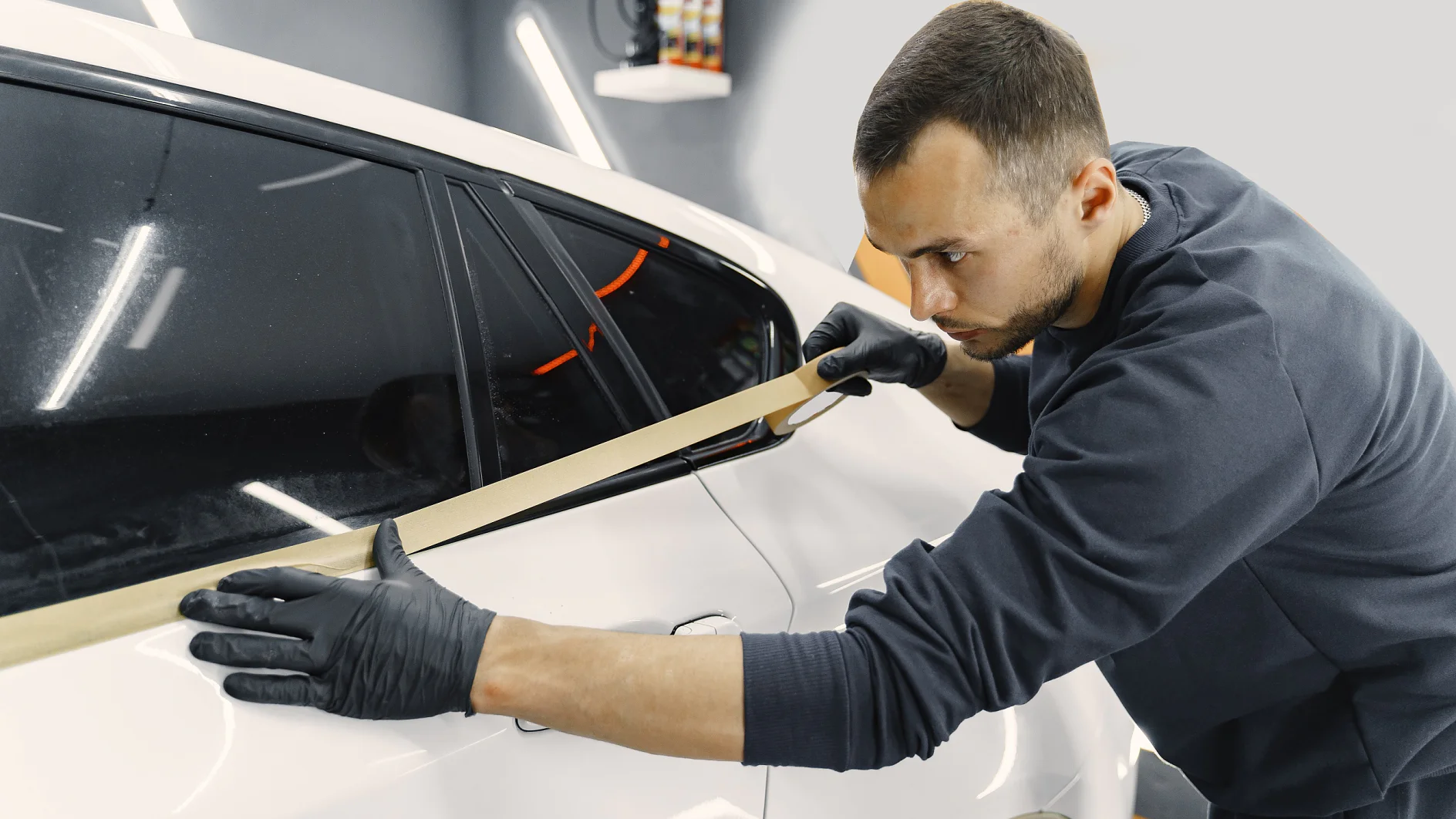 Auto body repair series. Masking car before repaint. Man in a black uniform.