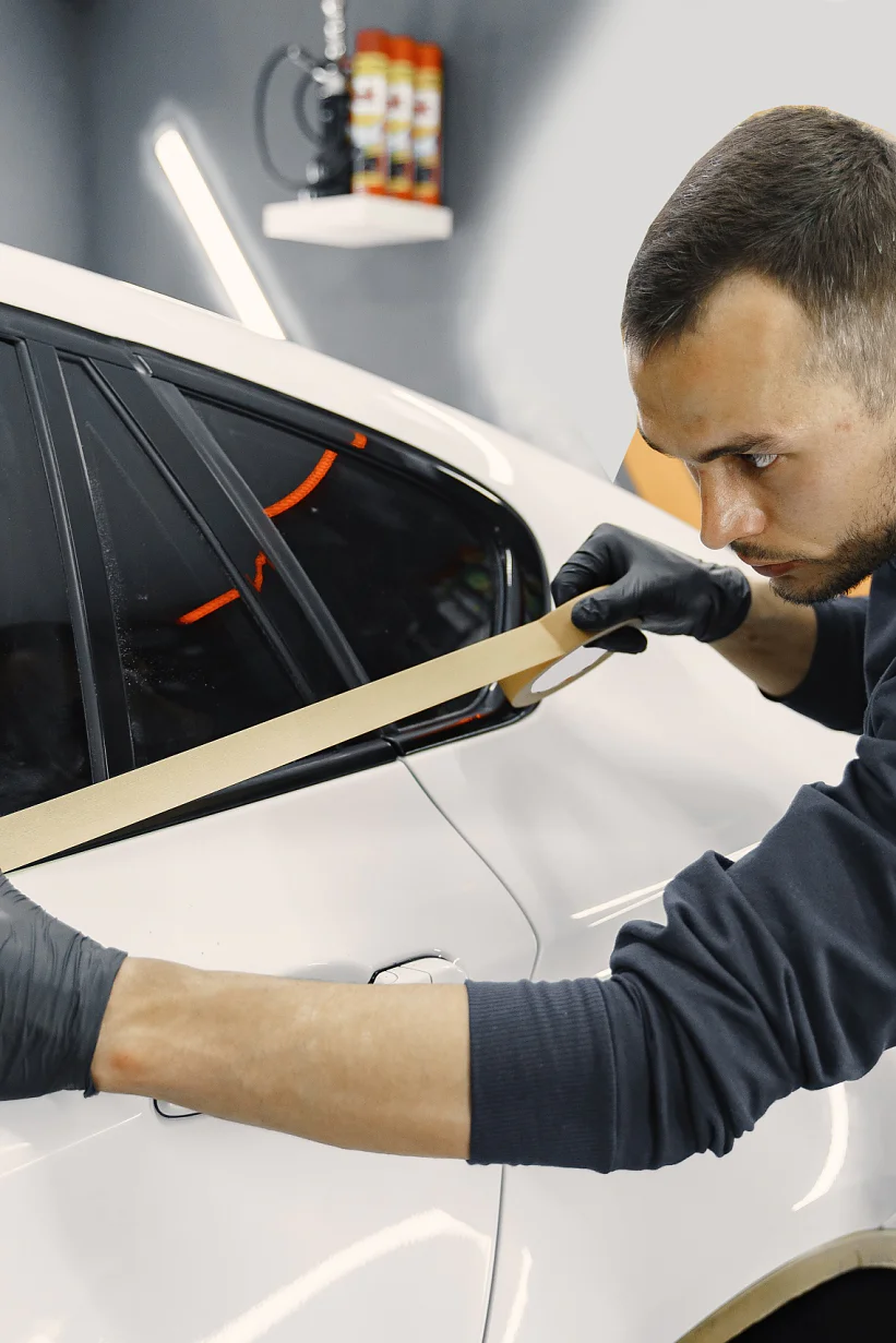 Preparing a car before spray painting Auto body repair series. Masking car before repaint. Man in a black uniform.