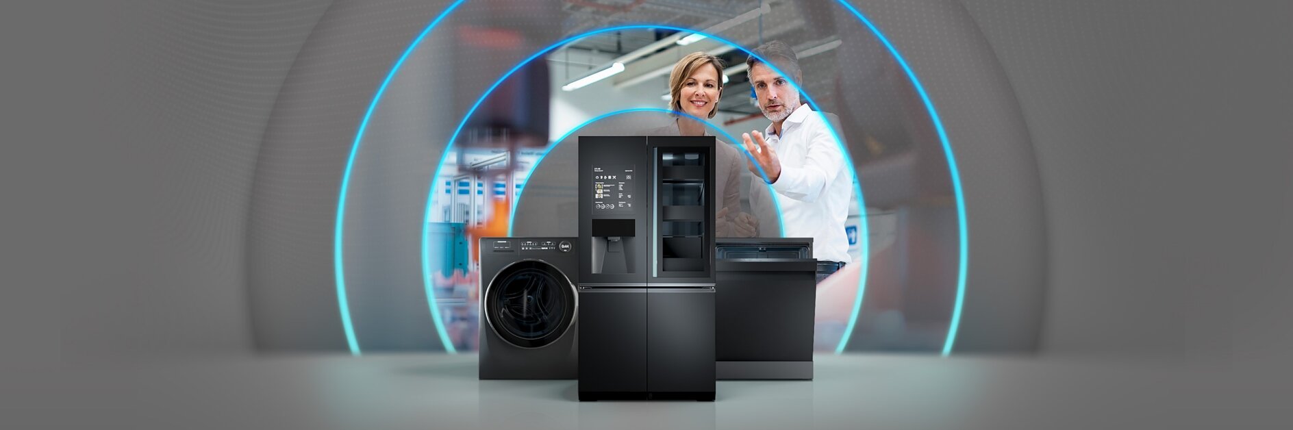 A man and woman discuss in front of a display featuring a black refrigerator, washing machine, and dishwasher. Blue light arches are visible in the background, creating a futuristic look. All around them are different types of tesa tape used to mount signs and secure cables in place. (This text has been generated by AI)