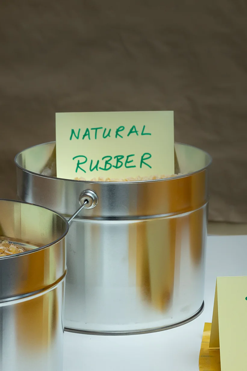 Metal containers labeled Resin and Natural Rubber hold raw materials. A tesa tape Liner sign is placed in front of yellow rolls on a table. (This text has been generated by AI)