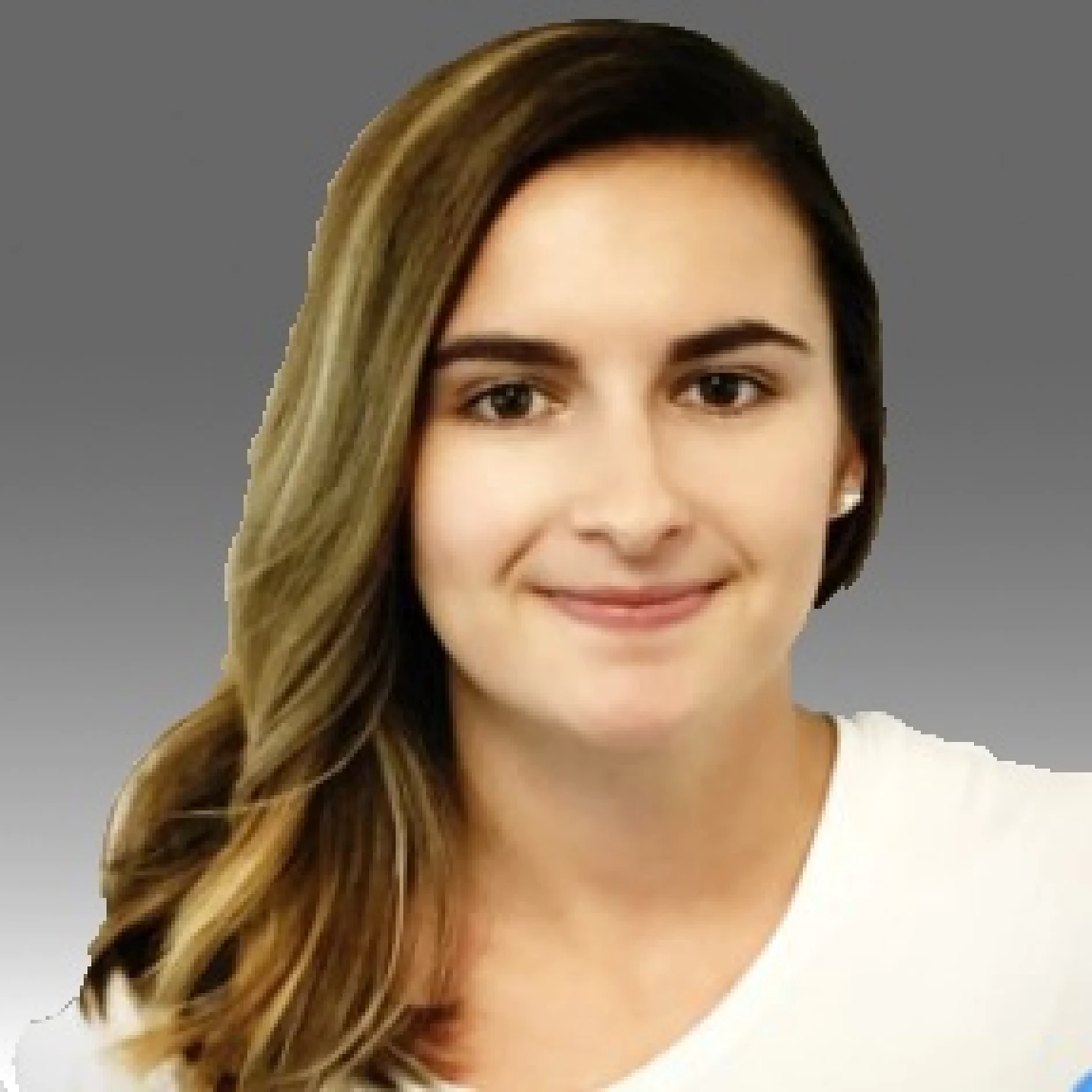 A person with long, straight brown hair is facing the camera and smiling slightly. They are wearing a white top. The background is a gradient of gray. (This text has been generated by AI)