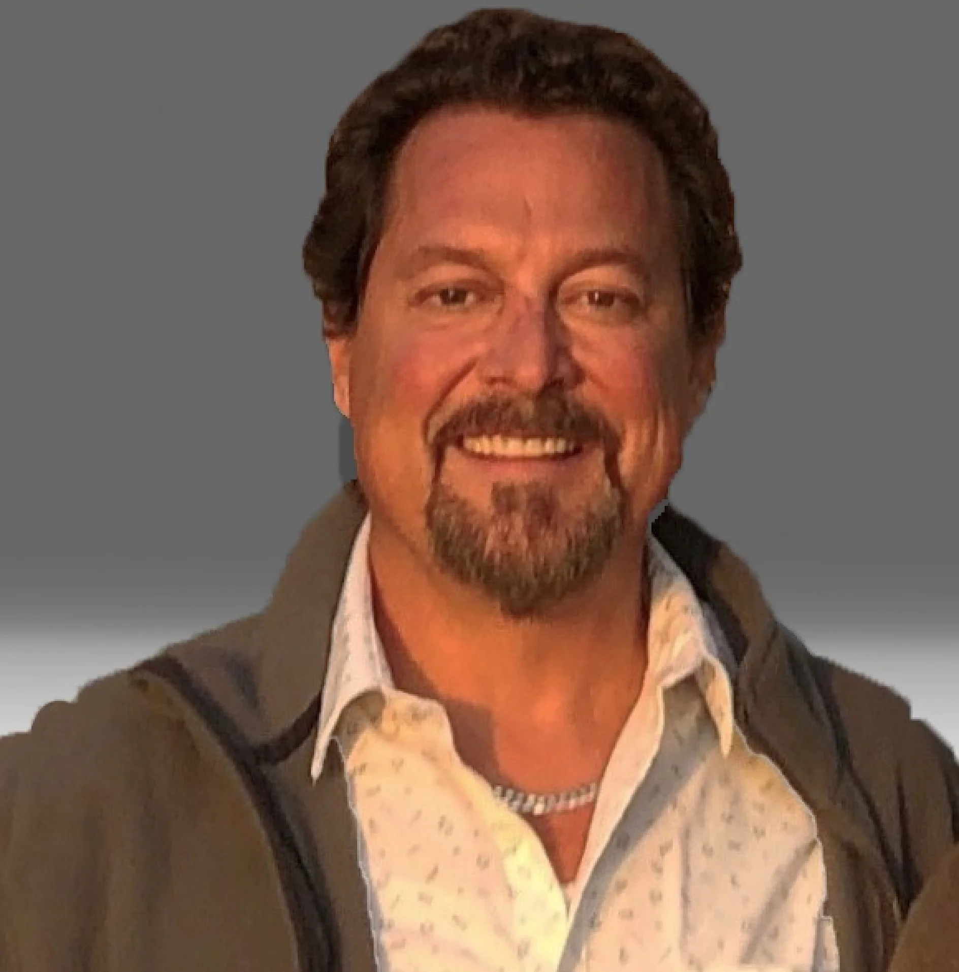 A man with short, curly brown hair and a beard smiles at the camera. He is wearing a light-colored shirt and a dark jacket. The background is a gradient of gray to light gray. (This text has been generated by AI)