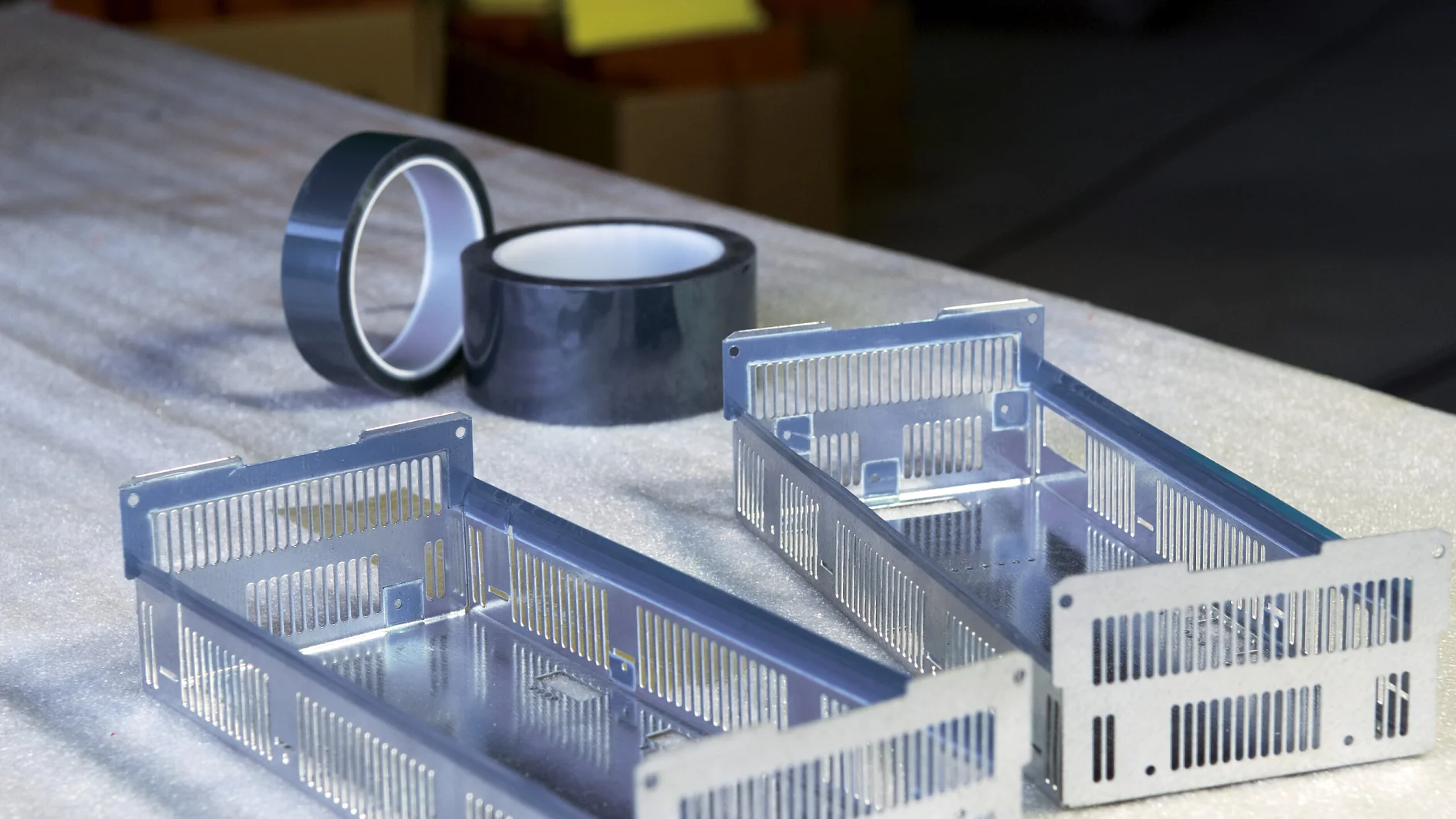 two metallic enclosures and rolls of tape are placed on a work surface. (This text has been generated by AI)