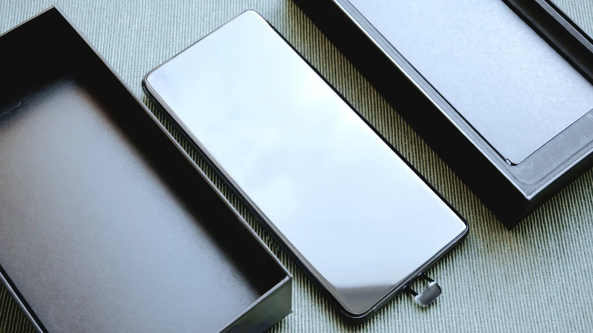 tesa smartphone with reflective screen placed between two open black boxes on a gray surface in an indoor setting (This text has been generated by AI)