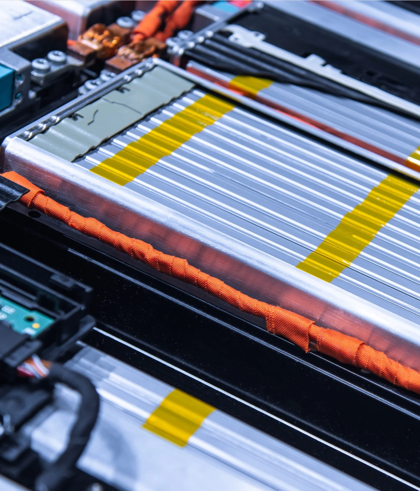 Close-up of a lithium-ion battery pack showing interconnected battery cells, orange electrical cables, and a visible circuit board within an electronic device or electric vehicle battery compartment, with tesa tape used for insulation and securing components. (This text has been generated by AI)
