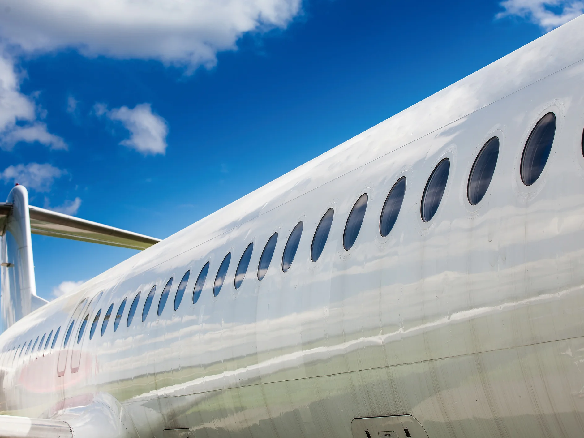 close-up of a silver airplane fuselage with oval windows under a blue sky with scattered clouds tesa (This text has been generated by AI)