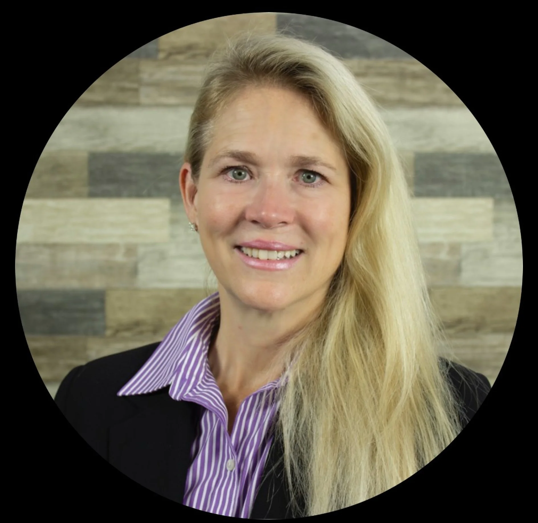 A woman with long blonde hair in a black blazer and striped shirt smiles; neutral wood panels are in the background. No tesa tape visible. (This text has been generated by AI)