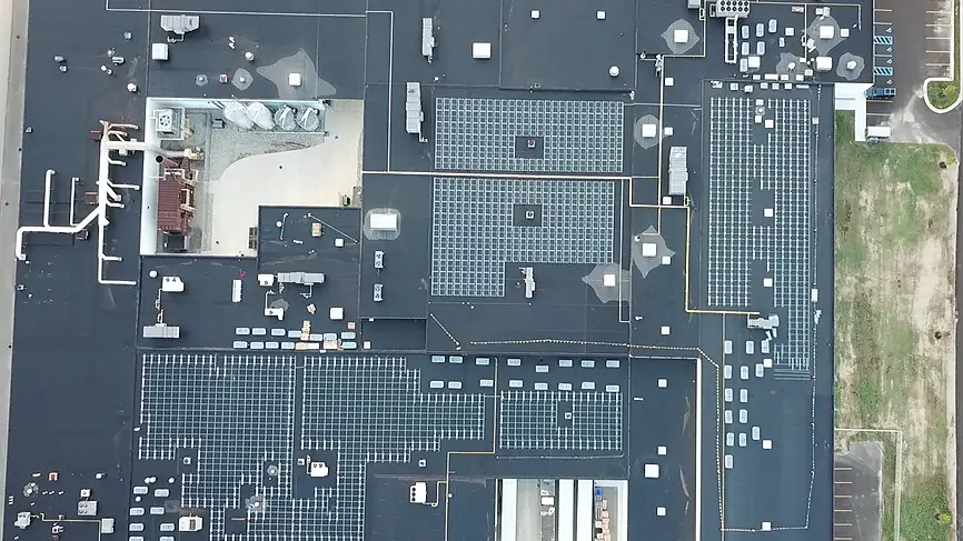 Aerial view of a large flat commercial roof with solar panels, HVAC units, skylights, and structures; tesa tape not visible.
