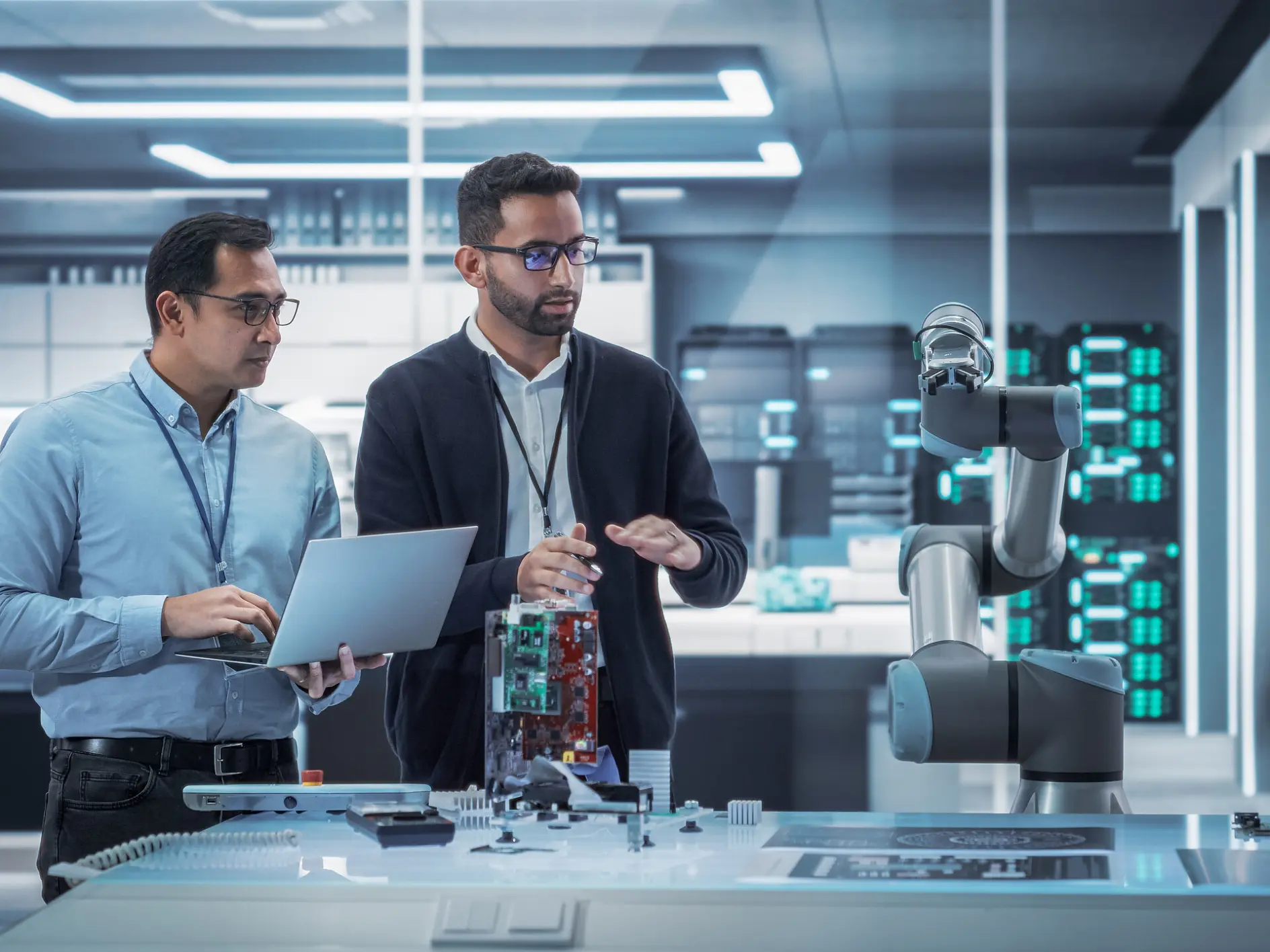 two engineers in a lab discuss a circuit board near a robotic arm in a high-tech indoor workspace tesa (This text has been generated by AI)