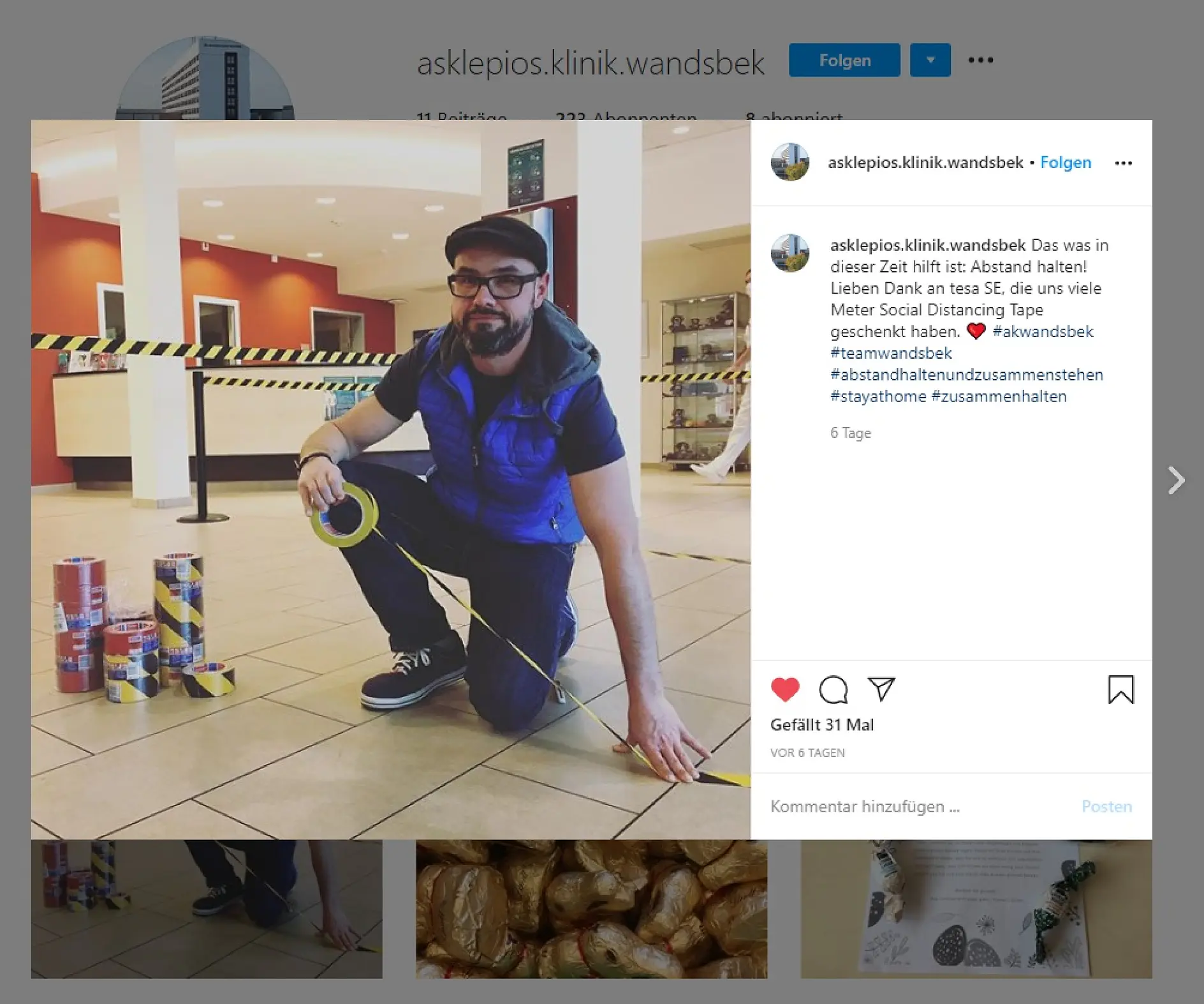 A man wearing glasses, a hat, and a vest is kneeling on a tiled floor, holding a roll of yellow tesa tape. Several rolls of tesa tape are stacked nearby. He is marking a line on the floor, likely for social distancing. A grocery store setting is visible.