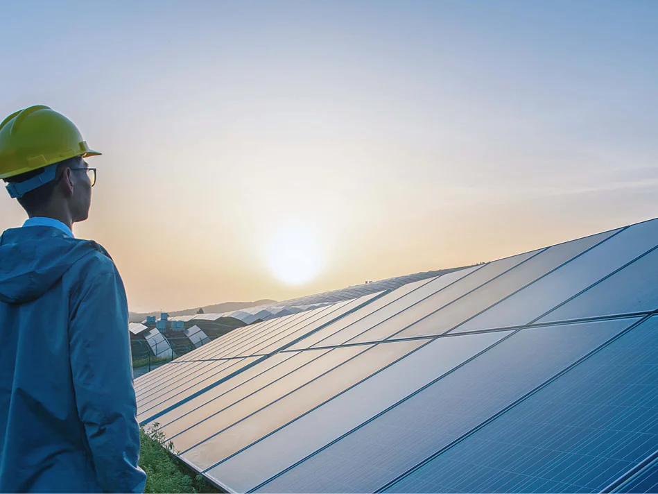 stage A person wearing a yellow hard hat stands in front of an array of solar panels at sunrise or sunset. The panels reflect the light, and the sky is clear. The individual is looking towards the horizon, holding a roll of tesa tape in their hand. (This text has been generated by AI)