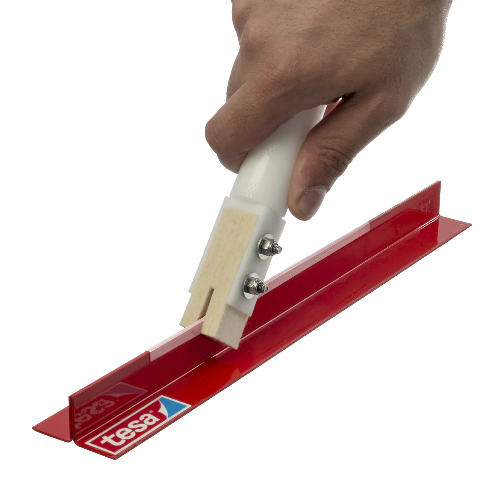A hand holding a tool with a white handle and a red base, pressing down on adhesive tesa tape. The word tesa is visible on the tape. The tool appears to be used for applying the tesa tape smoothly.