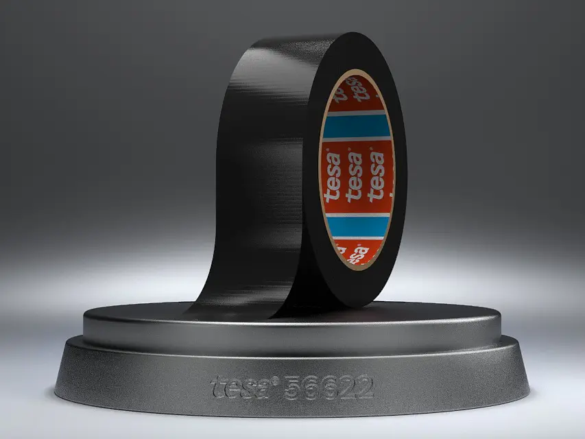 A roll of black adhesive tesa tape is partially unrolled on a round, gray pedestal. The tesa tape has a glossy finish, and the inner core is red with blue and white branding. The pedestal is inscribed with the text tesa® 56222. (This text has been generated by AI)