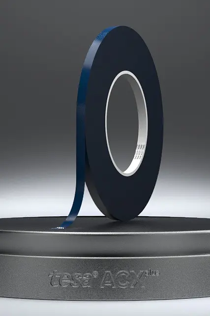 A roll of black adhesive tesa tape is displayed on a round, dark gray base against a gradient gray background. The edge of the tesa tape is slightly lifted. The base features the text VERSA LOOP at the front. (This text has been generated by AI)