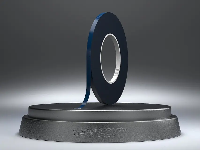 A roll of black adhesive tesa tape is displayed on a round, dark gray base against a gradient gray background. The edge of the tesa tape is slightly lifted. The base features the text VERSA LOOP at the front. (This text has been generated by AI)