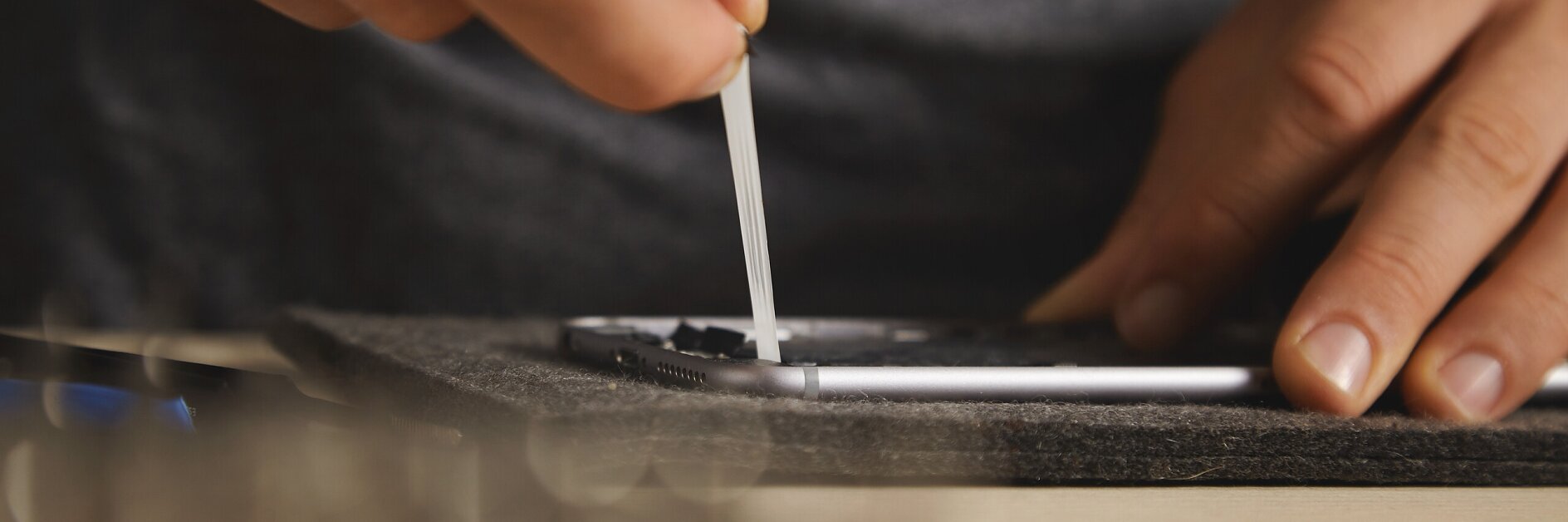 hands applying black adhesive tape to a surface using a small white stick, indoor workspace with focused activity tesa