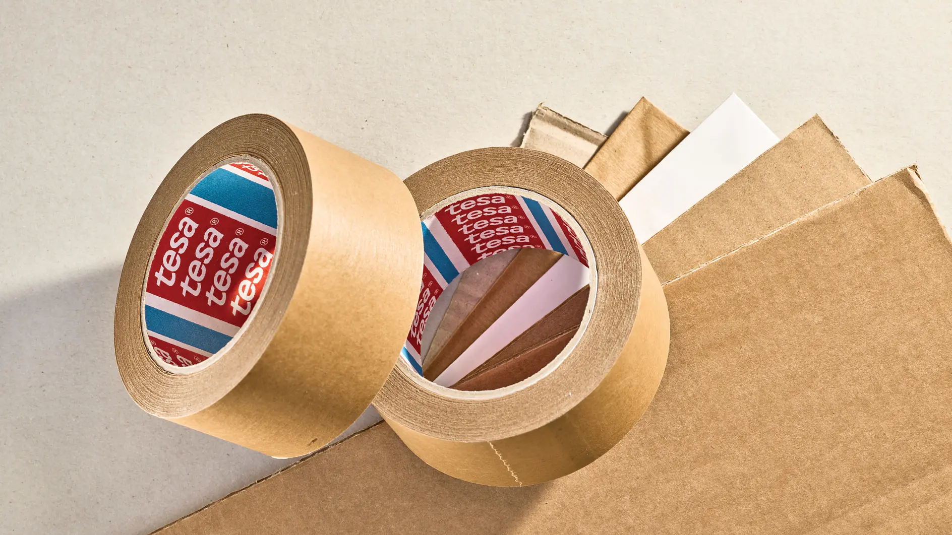 two rolls of tesa adhesive tape on a cardboard surface, one roll standing upright and the other lying on its side, indoor setting