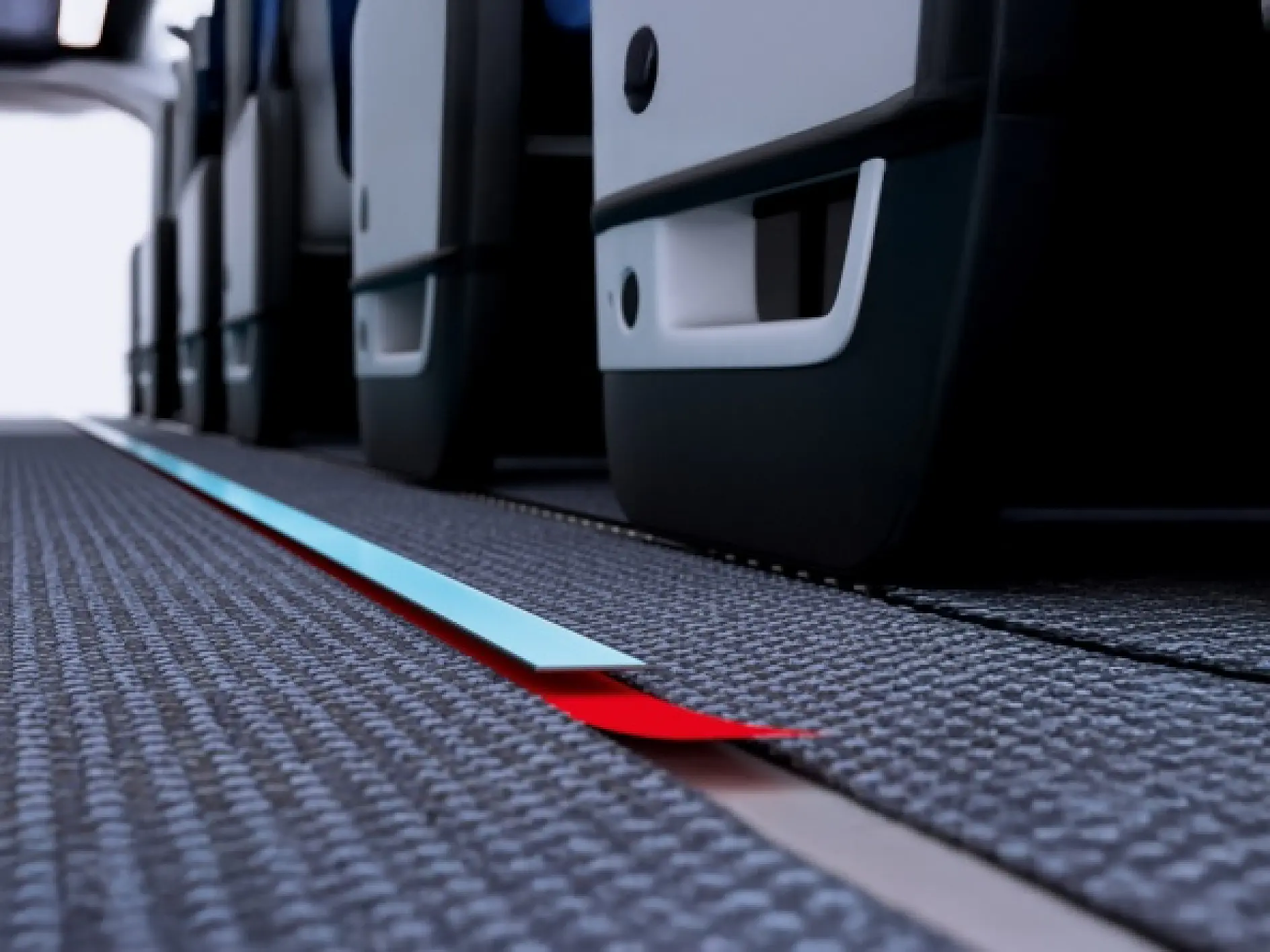 Close-up of an airplane cabin floor showing the aisle and rows of seats, with a red and blue illuminated tesa tape strip on the carpet.