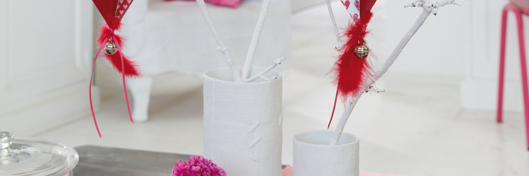 Homemade paper hearts hang in the bouquet made of branches painted white for Valentine's Day.