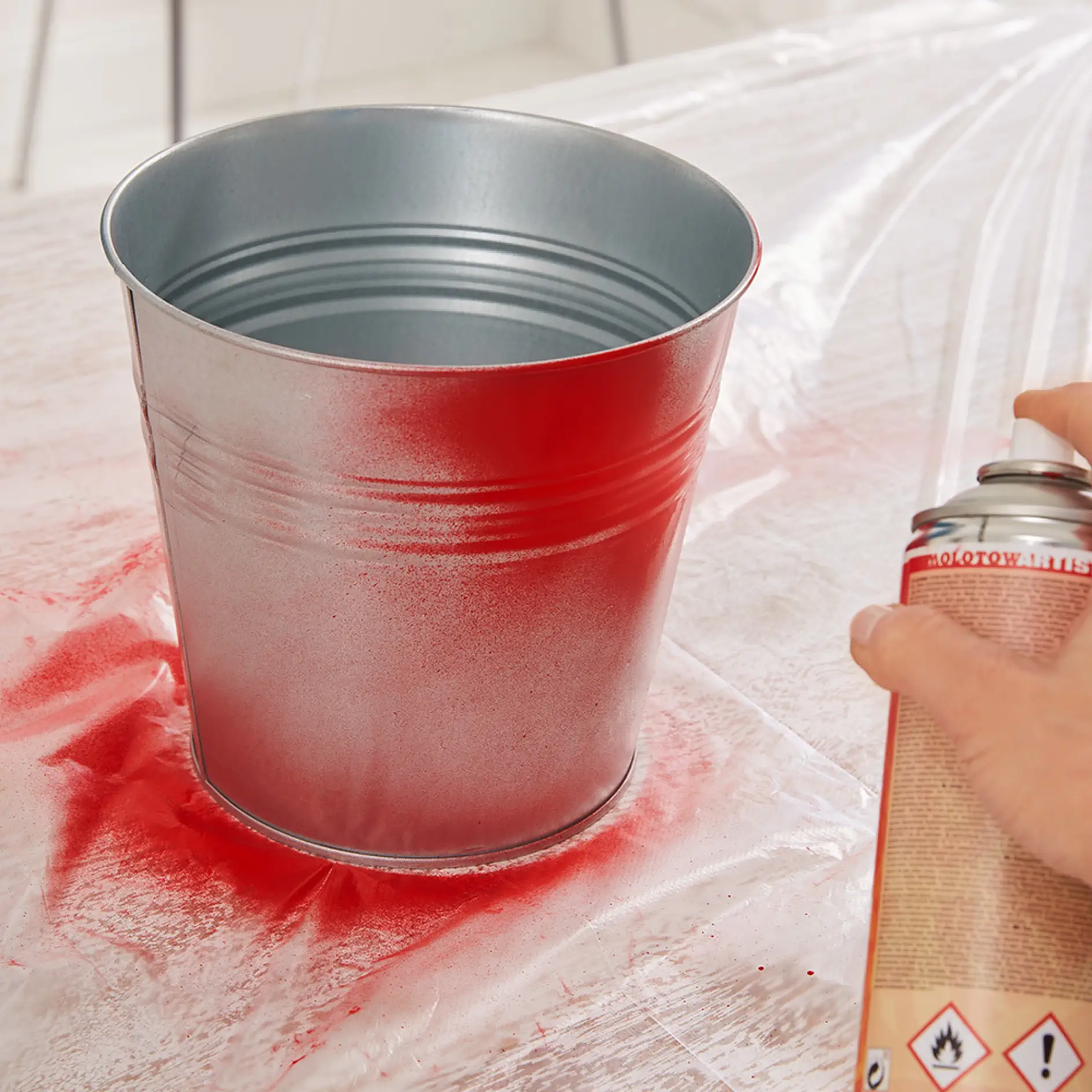 Painting a bucket when creating DIY garden hose storage using a drop cloth.