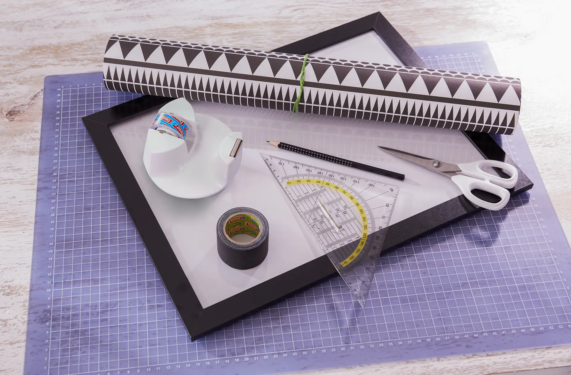 We need:
Basic photo frame with acrylic glass in desired size, Black-and-white wrapping paper, Protractor, Scissors, Pencil, tesa extra Power® ECO REPAIR, 5 m x 38 mm, black, tesafilm® desk dispenser Compact