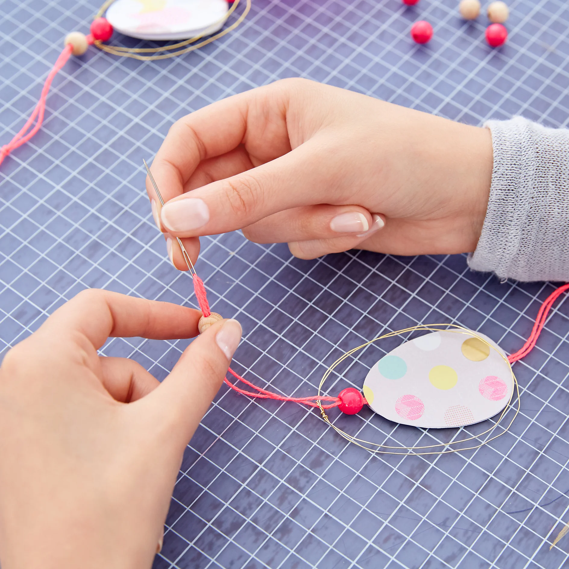 Thread a pink bead on the upper ends of the strings. Separate the strings and wrap them around the top of the wire egg. Draw both strings through another bead and make a knot.