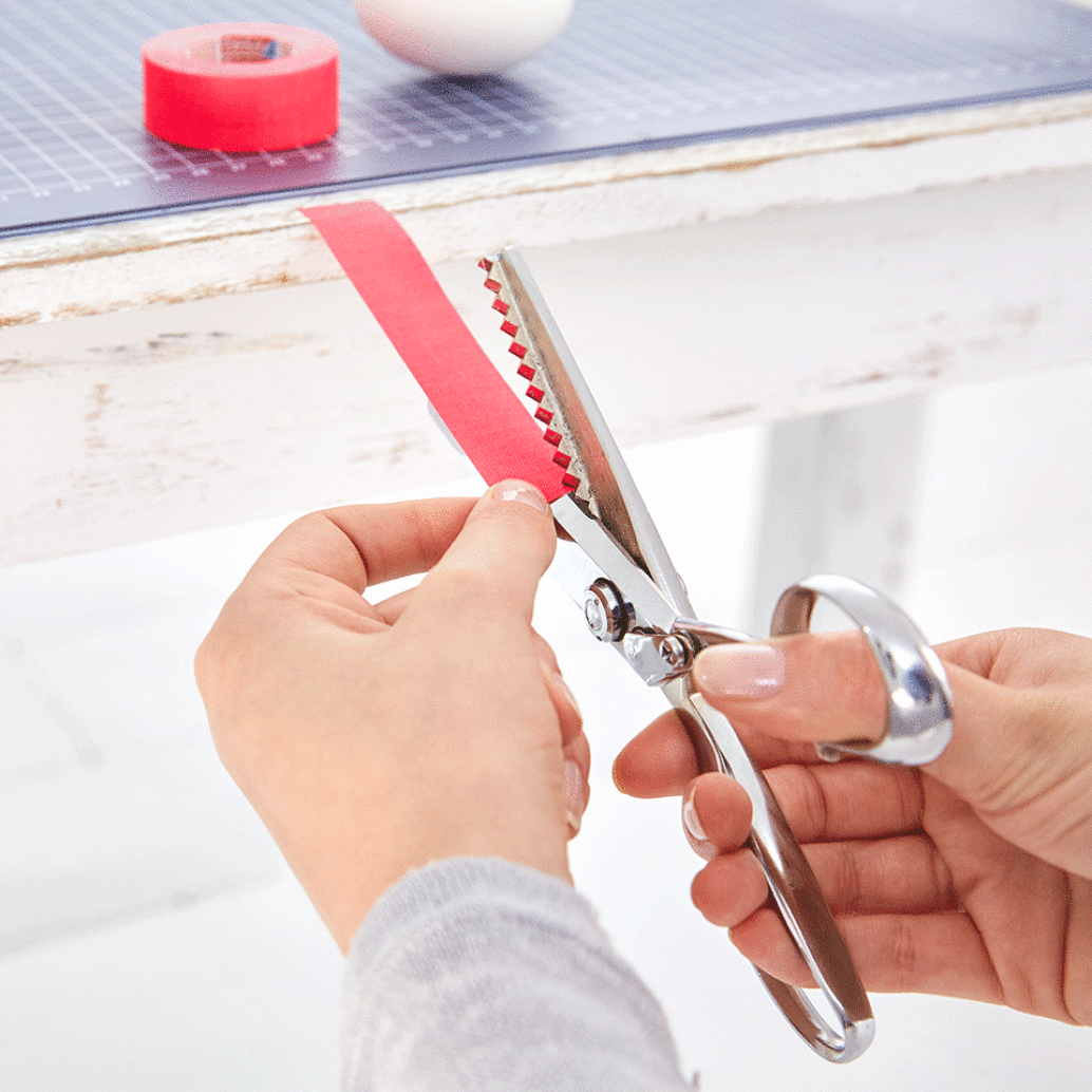 Cut the tape into thin strips using the pinking scissors. That works best when you attach the strip to the edge of the table and then cut it.