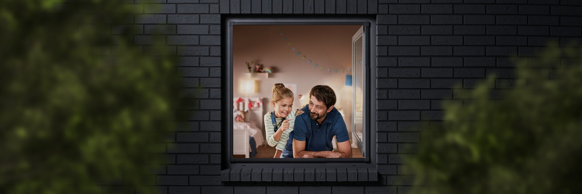 A man and a child are seen through a window, looking into a room decorated with colorful bunting. The building has dark brick walls, and the view is partially framed by blurred greenery. The man is wearing a blue shirt, and the child is sitting beside him. (This text has been generated by AI)