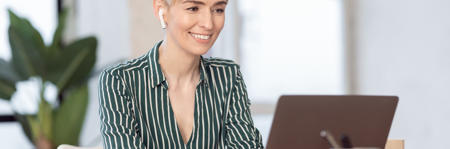 Mature Lady Working On Laptop In Earphones Sitting In Office