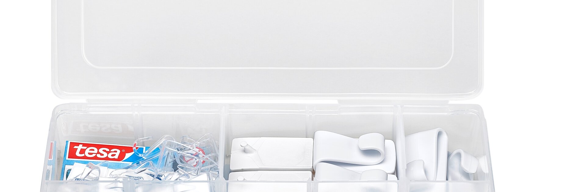 An organized plastic container with a transparent lid holds various white hooks and tesa tape adhesive strips in several compartments. tesa tape-branded adhesive strips and other small accessories are visible. (This text has been generated by AI)