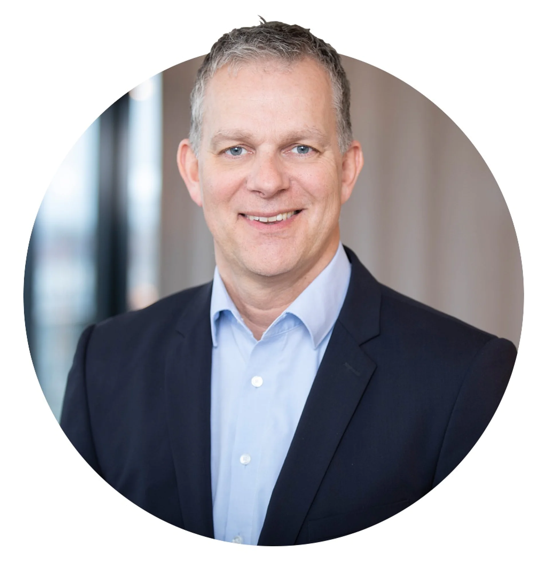 A man in a navy suit and light blue shirt is smiling at the camera. The background is softly blurred, suggesting an indoor setting. All references to tape have been replaced with tesa tape. (This text has been generated by AI)