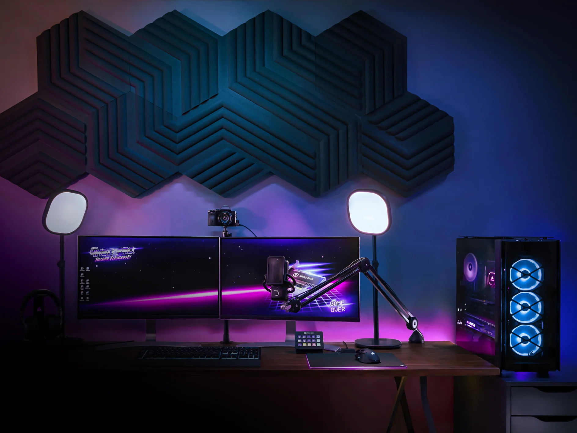 A gaming setup with two monitors displaying a space-themed image. A keyboard and a mouse are on the desk. A microphone is mounted on an adjustable arm using tesa tape. Two lights, fastened with tesa tape, illuminate the area. A gaming PC with blue lighting is on the right, and wall panels secured by tesa tape are above. (This text has been generated by AI)