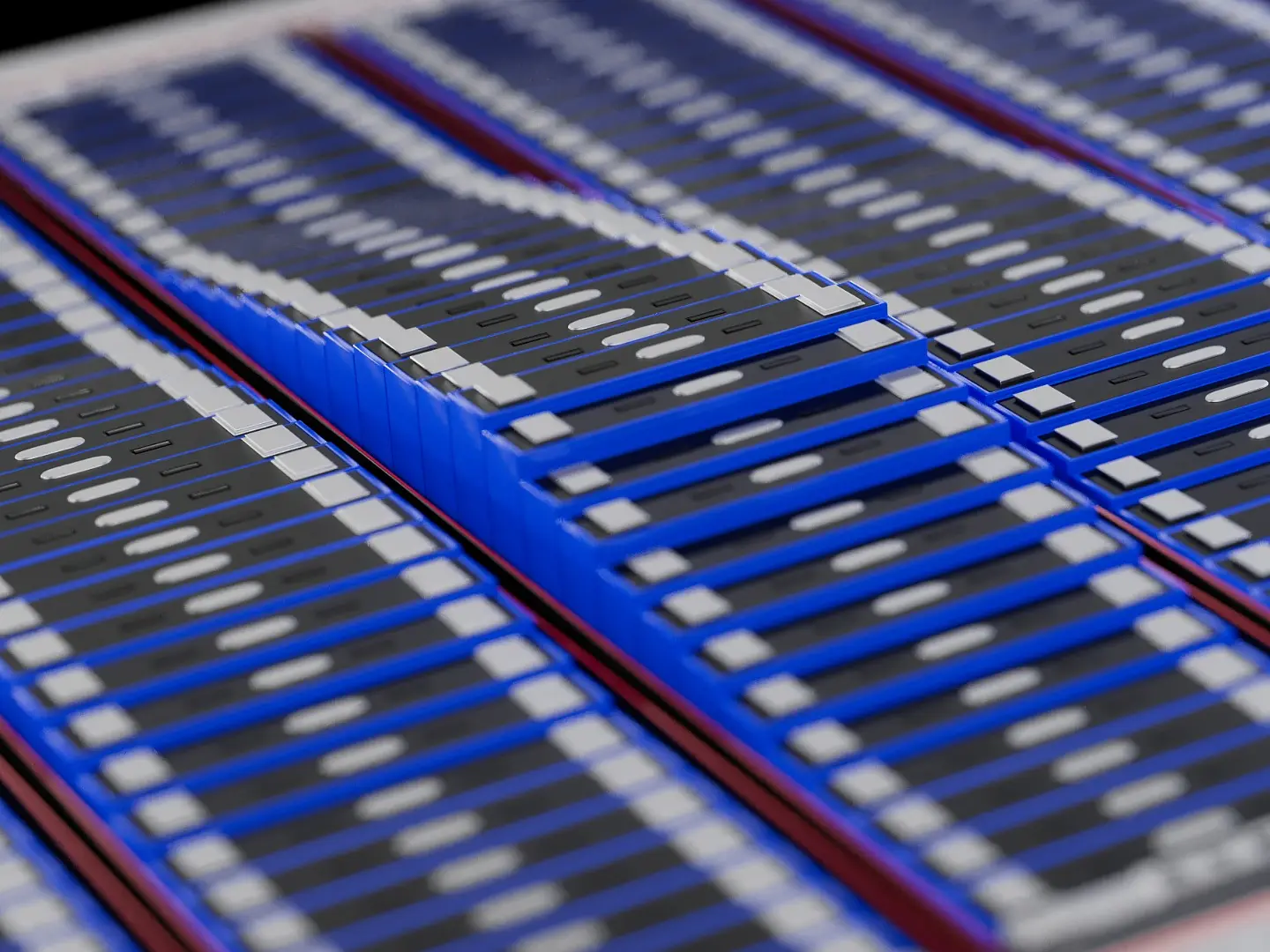 A close-up view of rows of rectangular blue objects with black tops and white horizontal details, resembling electronic components or battery cells, arranged in a slightly curved pattern, with some featuring tesa tape. (This text has been generated by AI)