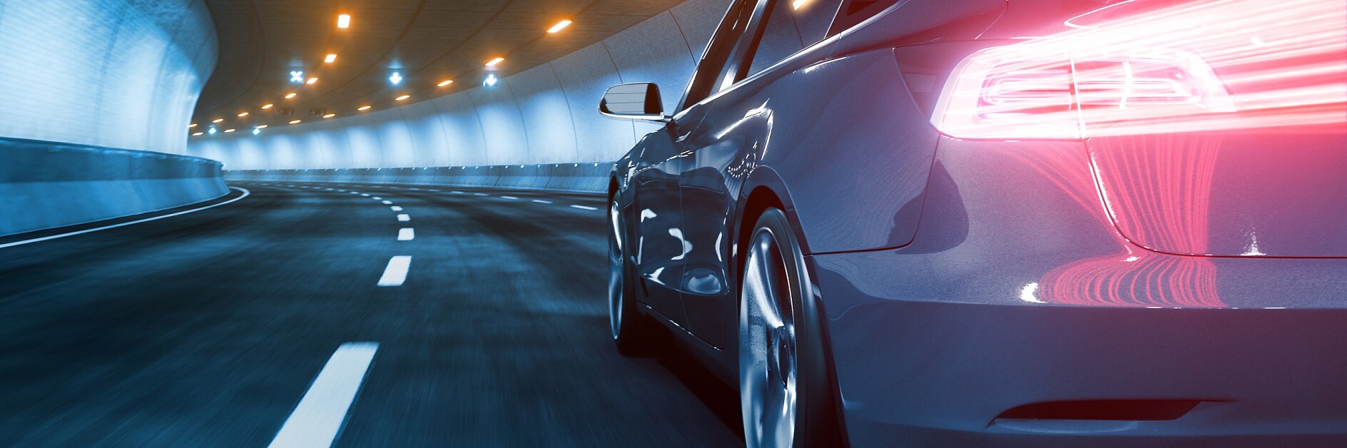 A sleek car with illuminated taillights speeds through a well-lit tunnel. The road is marked with dashed white lines, and the surrounding walls are light blue. The tunnel is equipped with overhead lights and is curving to the left.