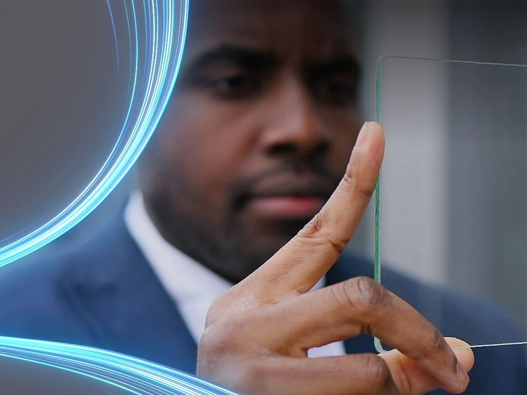 A person in a suit holds a transparent piece of tesa tape between their fingers, examining it closely. Blue glowing lines curve around the left side of the image, adding a futuristic element. (This text has been generated by AI)