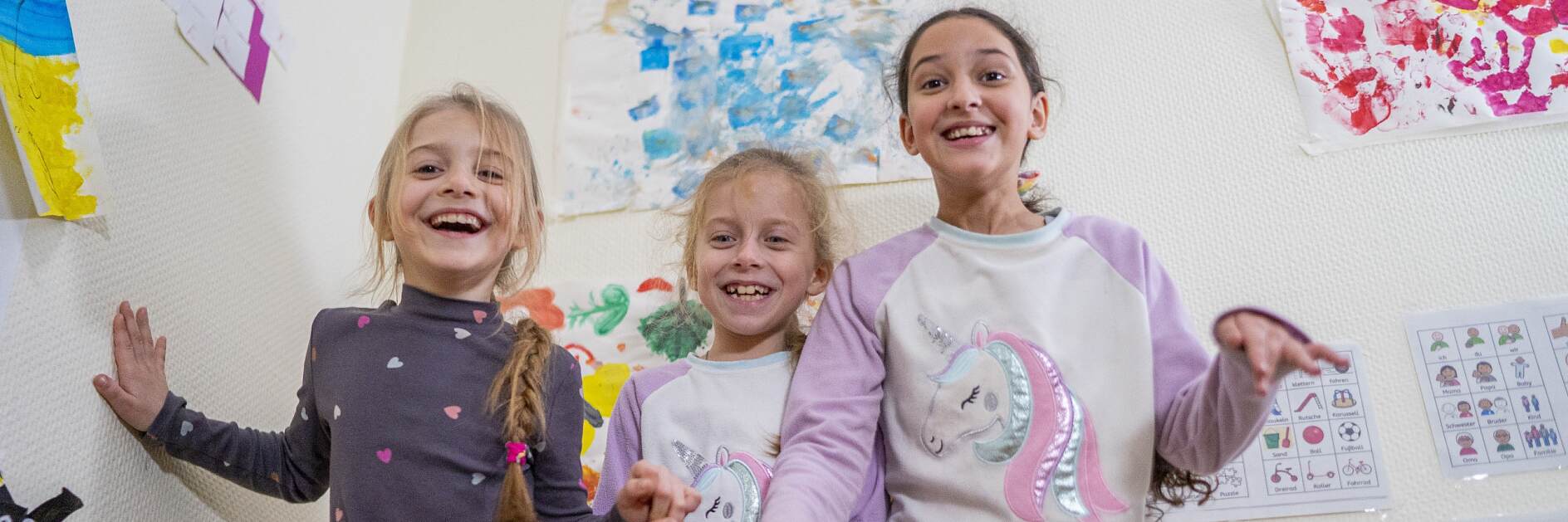 (From left to right) Larissa*, 7, Svitlana*, 7 and Daniela*, 11 smile at the camera in the Child Friendly Space located in a temporary shelter for Ukrainian refugees in Frankfurt, Germany.