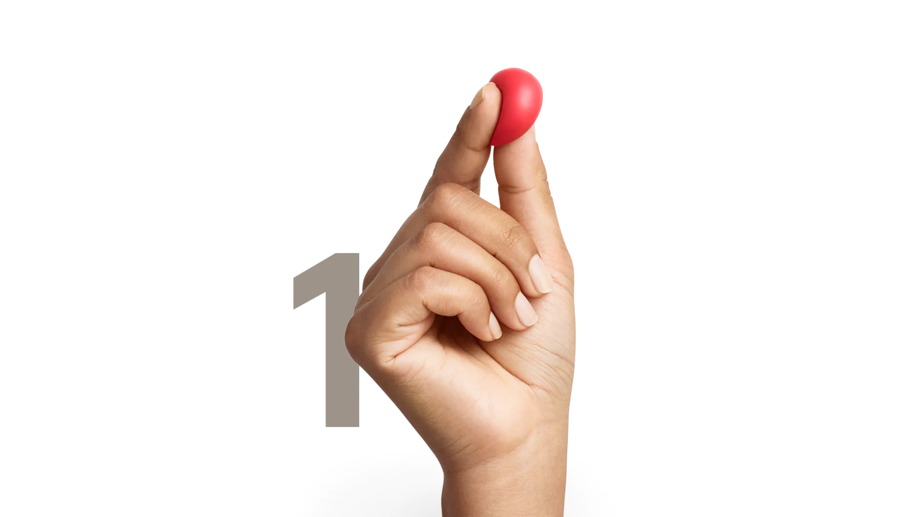 A persons hand holding a small, red, oval-shaped object between their thumb and index finger. A large numeral 1 is visible in the background. (This text has been generated by AI)