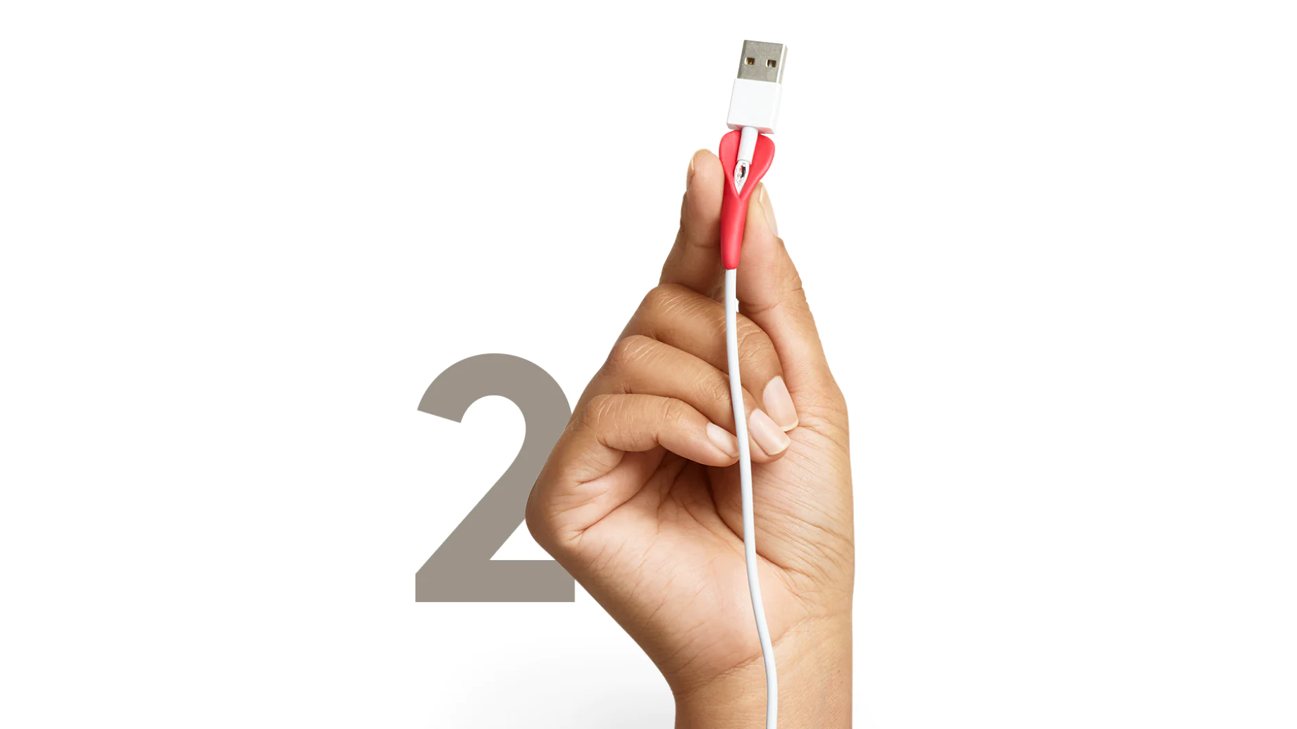 A hand holding a USB cable with a red plastic grip is shown against a white background. The cable is positioned vertically, and a large gray number 2 is visible in the background, secured with tesa tape. (This text has been generated by AI)