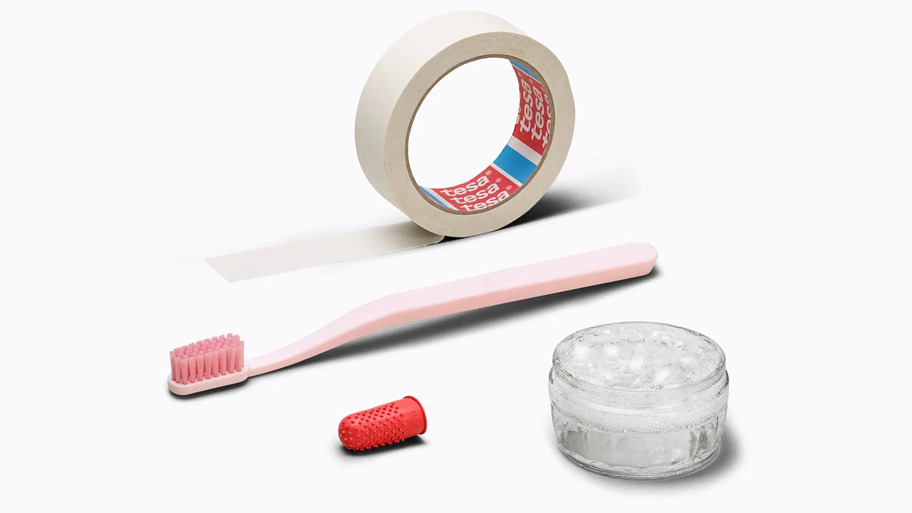 materials_mobile_tape A roll of masking tesa tape, a pink toothbrush, a small glass jar with clear substance, and a red thimble are arranged on a white background. (This text has been generated by AI)