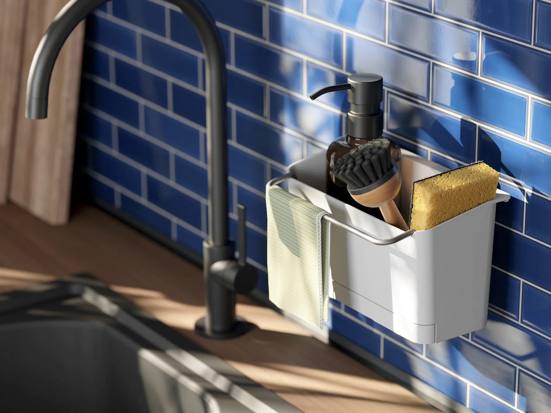 A kitchen scene shows a matte black faucet over a stainless steel sink. A container attached to the blue-tiled backsplash holds a soap dispenser, a scrubbing brush, and a sponge. A cloth hangs on the container, held securely in place with tesa tape, and sunlight casts shadows. (This text has been generated by AI)