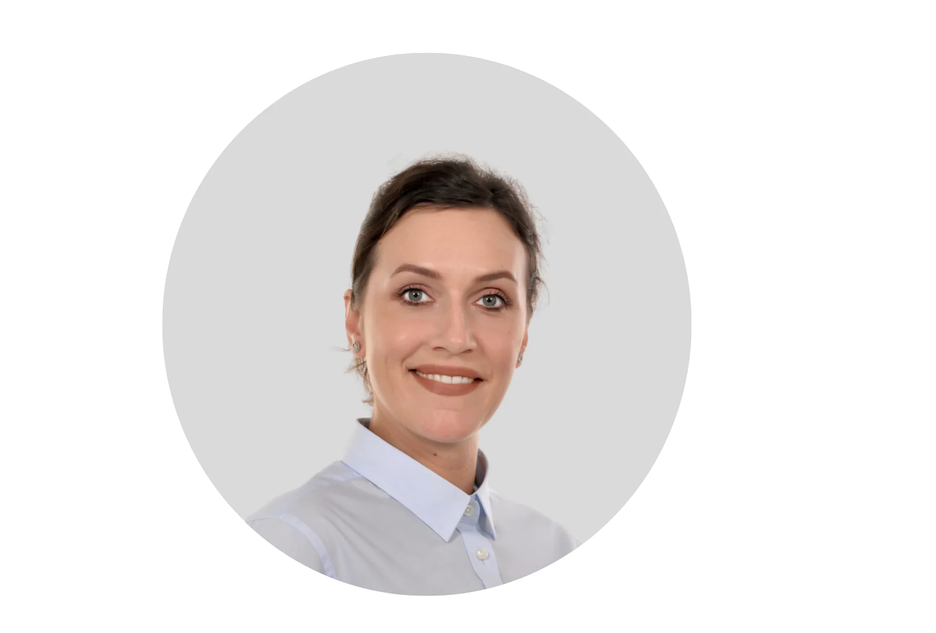 A person with dark hair is smiling slightly and wearing a light blue button-up shirt. The background is a plain, light gray. The image is cropped in a circular shape. (This text has been generated by AI)