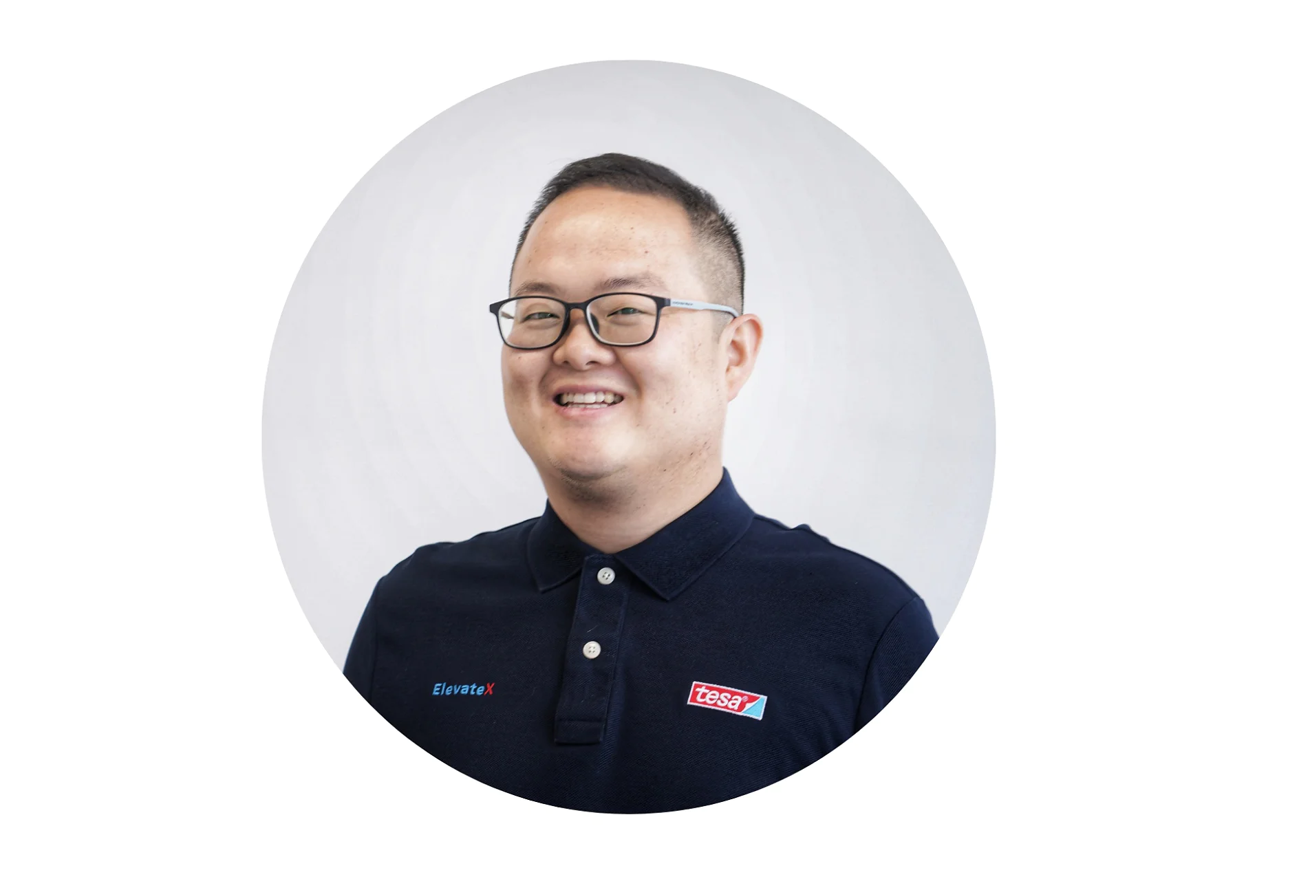 A person wearing glasses and a navy polo shirt with logos Elevate and tesa tape smiles against a light gray background. (This text has been generated by AI)