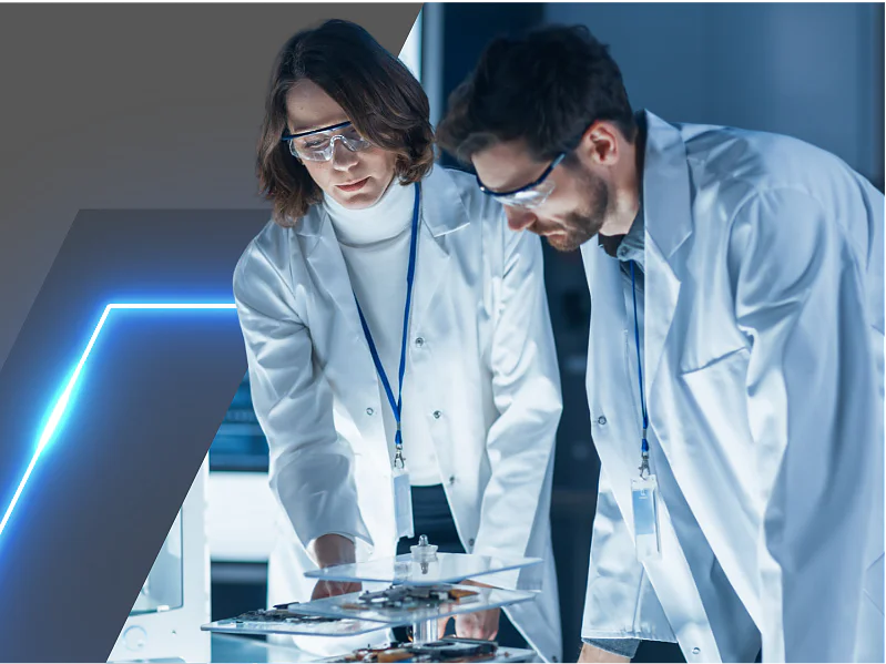 Two scientists wearing white lab coats and safety goggles work together in a lab. They are examining equipment on a table. The background features a geometric design with a blue light accent on the left side, and they are using tesa tape for their experiments. (This text has been generated by AI)