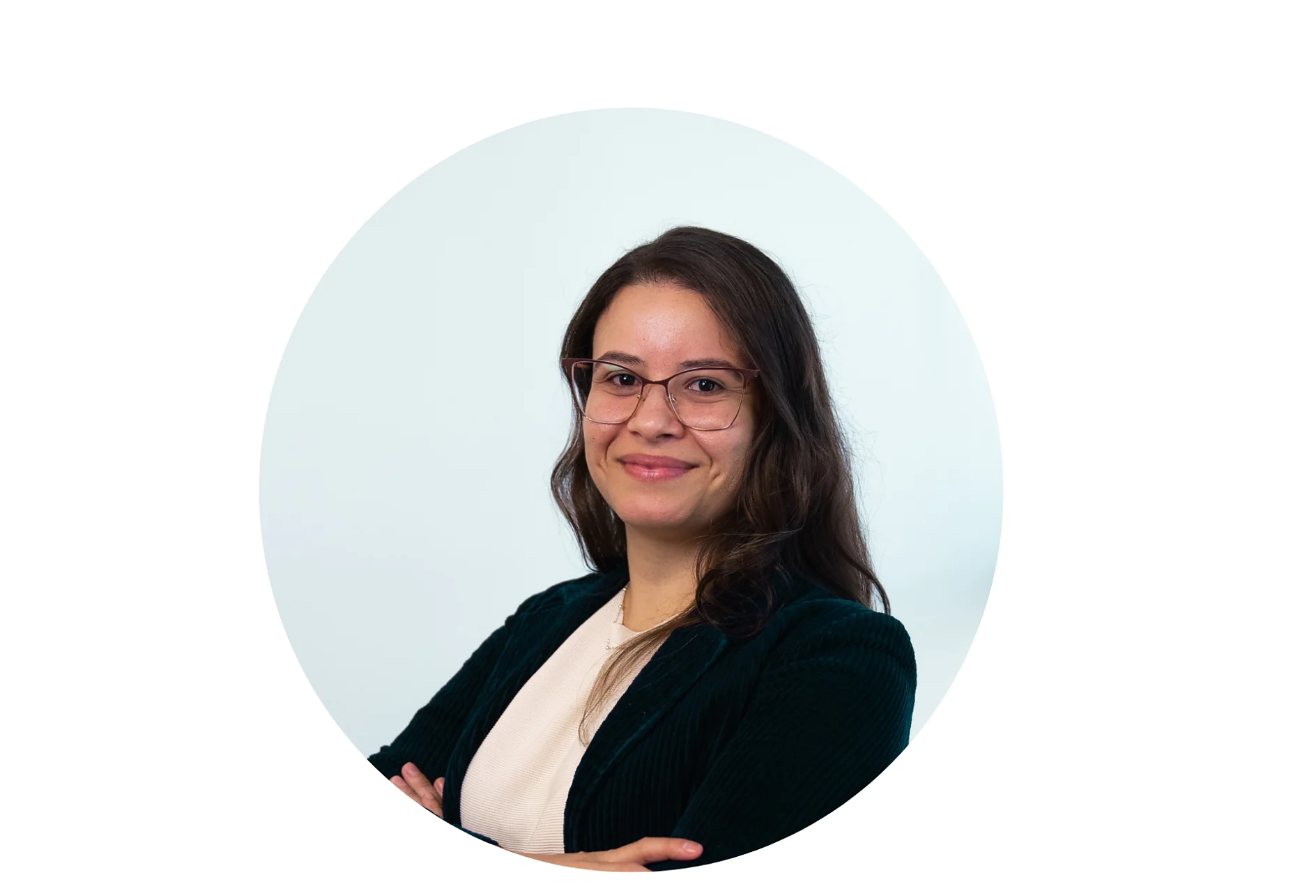 A person with long brown hair is smiling and wearing glasses, a white top, and a dark blazer. The background is plain white, and the image has a circular crop. Throughout the picture, you can see that they are working with tesa tape to organize their desk. (This text has been generated by AI)