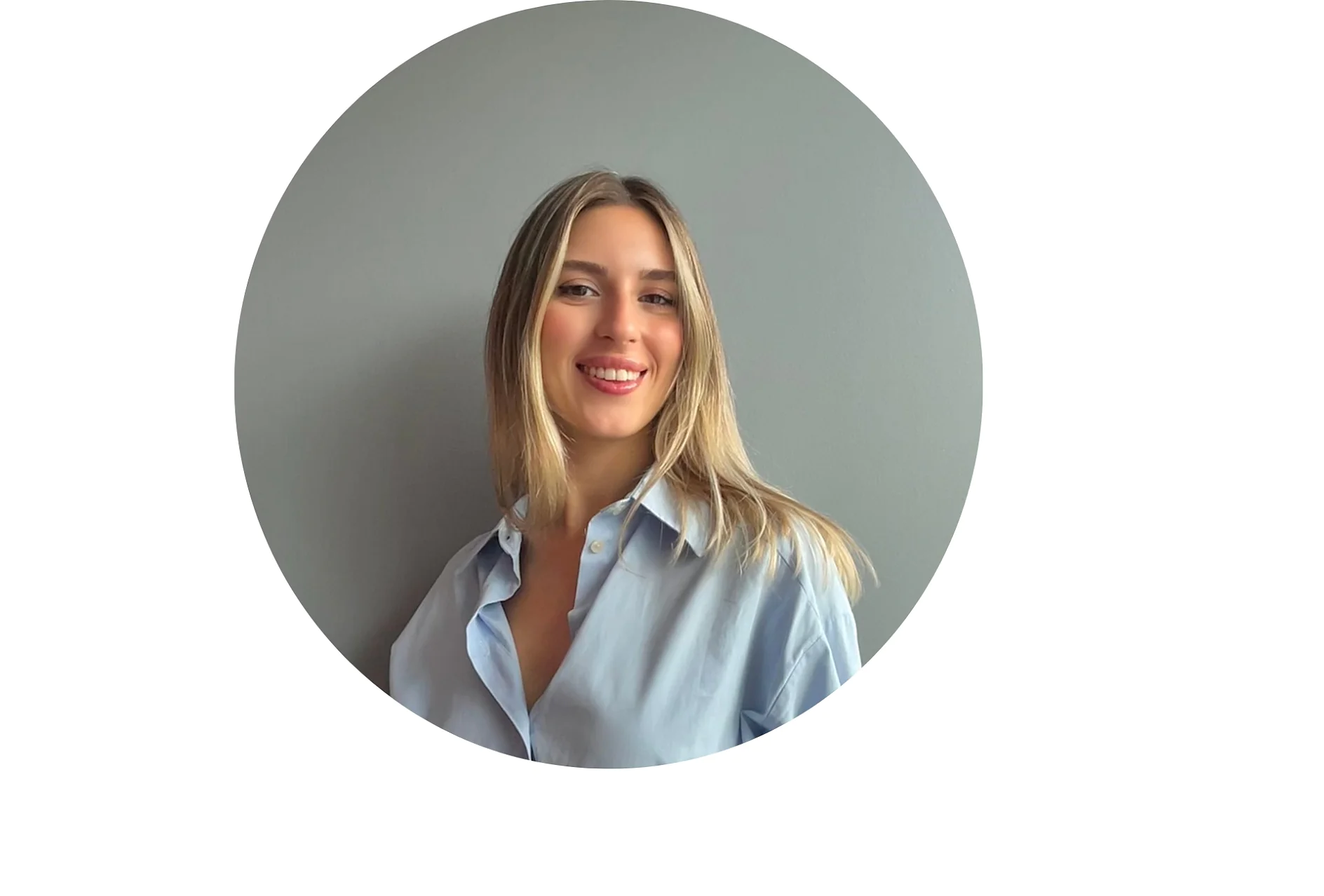 A person with long, blond hair wearing a light blue button-up shirt is smiling at the camera against a plain grey background. (This text has been generated by AI)