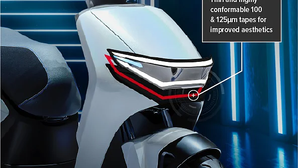 Close-up of a white scooters front section with layered tesa tape designs on the headlight. A label points to the headlight, noting “Thin and highly conformable 100 & 125μm tesa tapes for improved aesthetics.”. (This text has been generated by AI)
