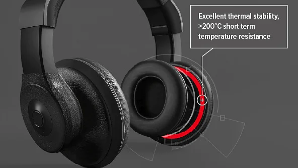 A pair of black over-ear headphones with a highlighted red inner ring, accompanied by text stating: “Excellent thermal stability, >200°C short term temperature resistance with tesa tape.” The background is plain gray. (This text has been generated by AI)