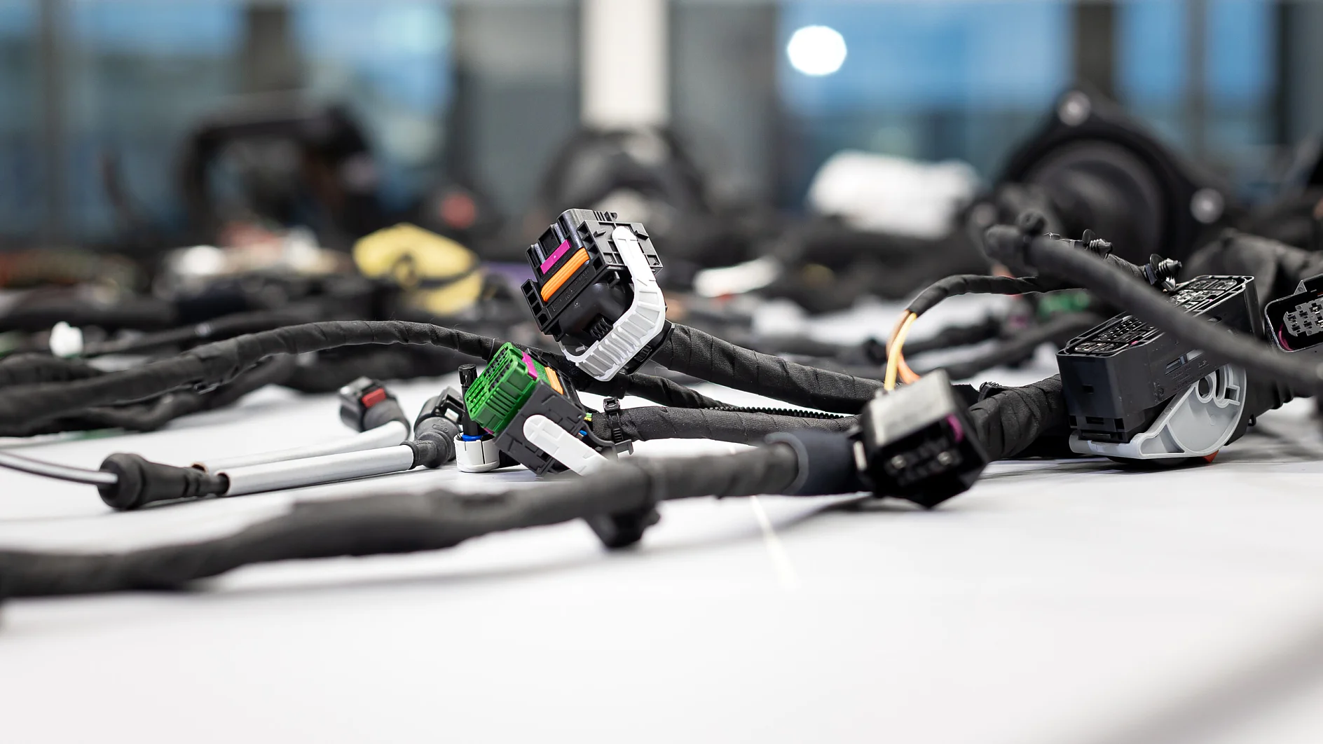 Several wiring harnesses with connectors and cables, wrapped in tesa tape, are laid on a white surface; blurred indoor background. (This text has been generated by AI)