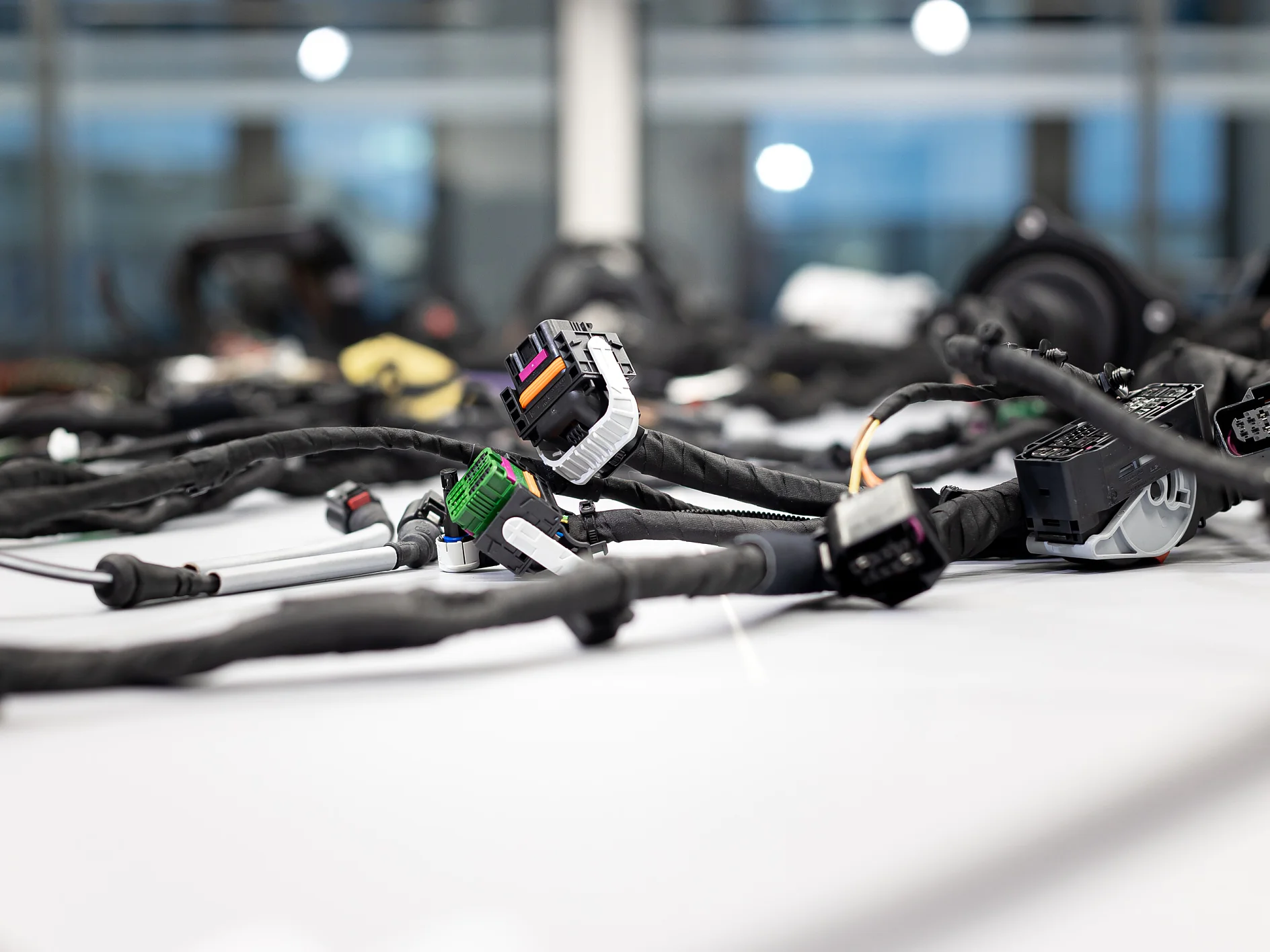 Several wiring harnesses with connectors and cables, wrapped in tesa tape, are laid on a white surface; blurred indoor background. (This text has been generated by AI)